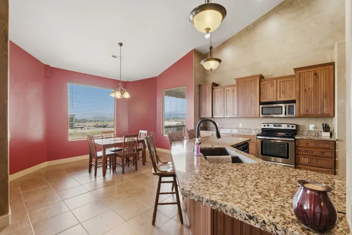 Kitchen featuring a granite-topped island with an undermount sink, wood cabinetry, stainless steel appliances, and tile flooring