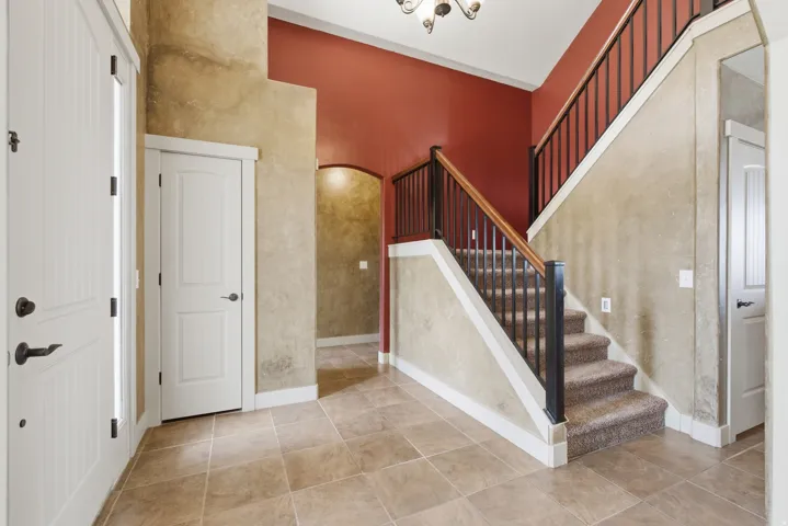 Entryway featuring tile flooring, a carpeted staircase with dark iron balusters and wood handrail, and high ceilings