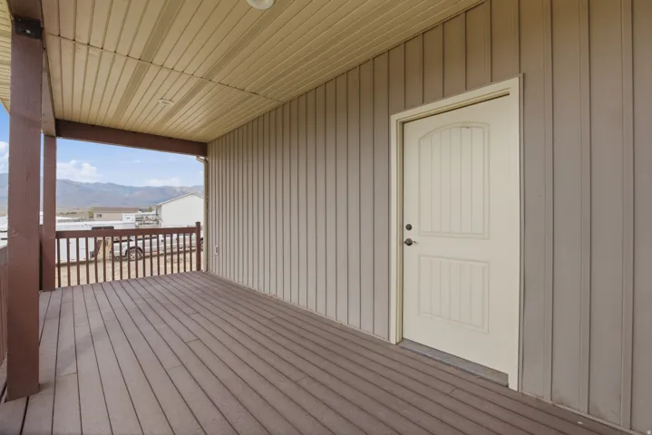 Covered porch featuring a wood-finish deck, brown railing, and beige vertical siding