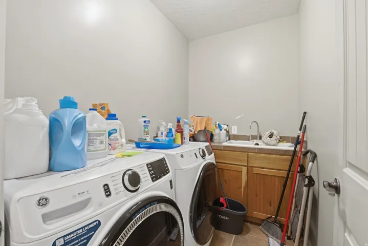 Laundry room featuring a utility sink, light wood cabinetry, and neutral tile flooring