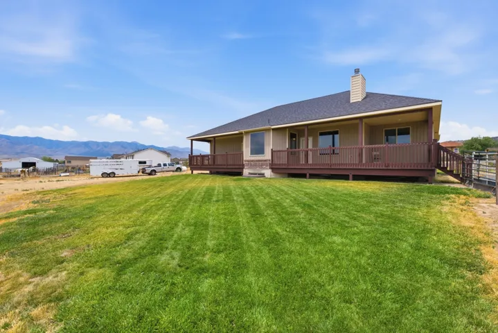Expansive green lawn with a tan exterior residence featuring a covered deck, dark brown railing, and an exterior chimney