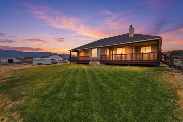 Expansive rear yard featuring a manicured lawn, a full-length covered deck, and a wood railing with stairs