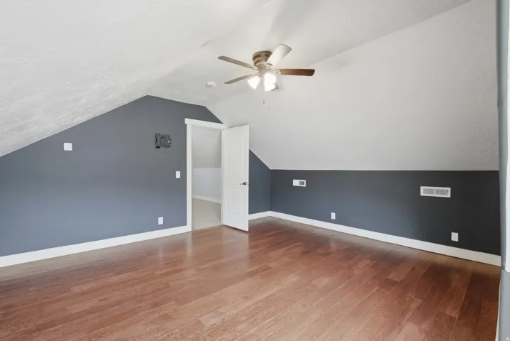 Spacious room featuring wood-finish flooring, a ceiling fan, and sloped ceilings