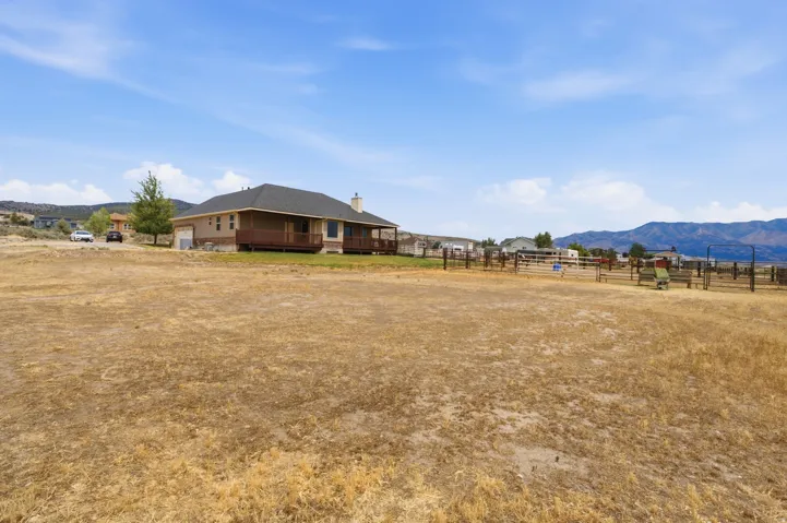 Expansive land parcel featuring a ranch-style home with a dark shingle roof and a full-length wooden deck