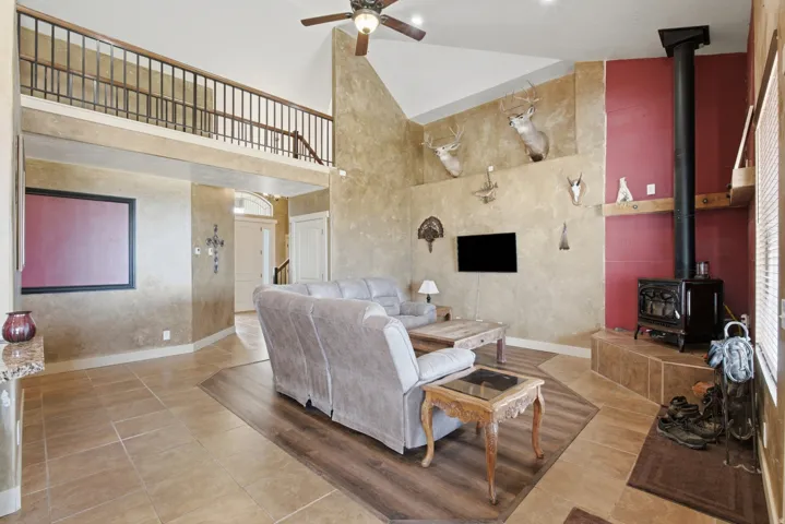 Vaulted living space with a loft, featuring a corner wood-burning stove on a tiled hearth, mixed flooring with large format tiles and wood-finish planks, and a ceiling fan