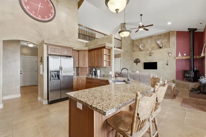 Kitchen featuring a granite countertop island with integrated sink, wood cabinetry, stainless steel refrigerator, and tiled flooring
