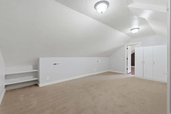 Carpeted room featuring vaulted ceilings, built-in shelving, white walls, and built-in white cabinetry with silver hardware