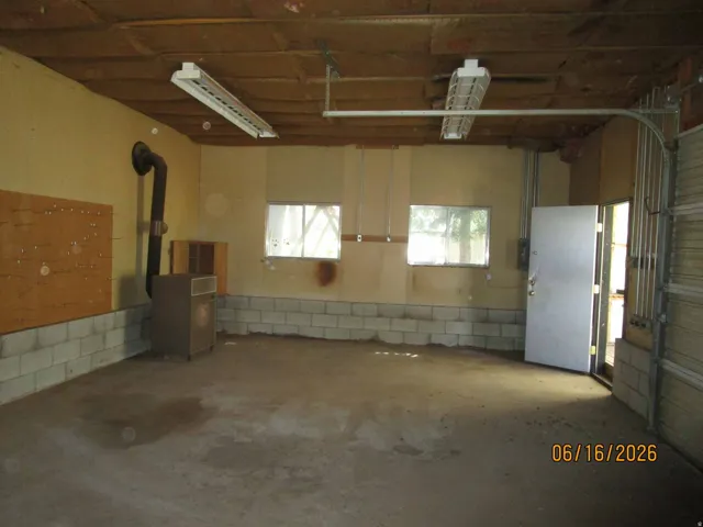 Spacious garage interior featuring exposed wood ceiling beams, concrete block wainscoting, and a concrete floor