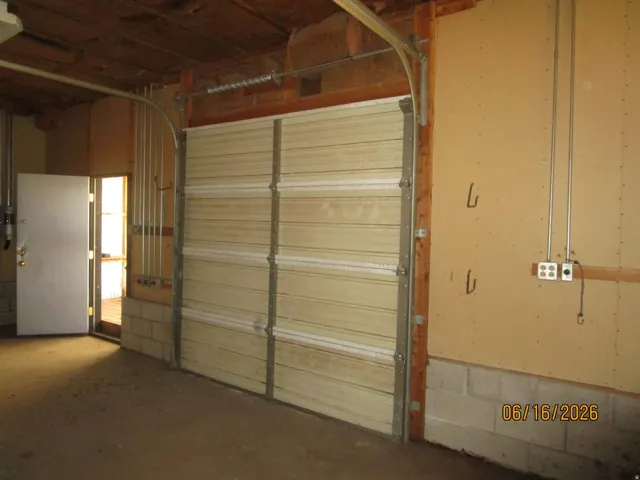 Garage interior featuring a sectional garage door, concrete flooring, exposed ceiling joists, and a utility door