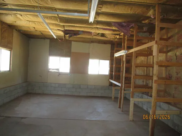 Spacious interior featuring a concrete slab floor, exposed ceiling insulation, fluorescent lighting, and multiple windows