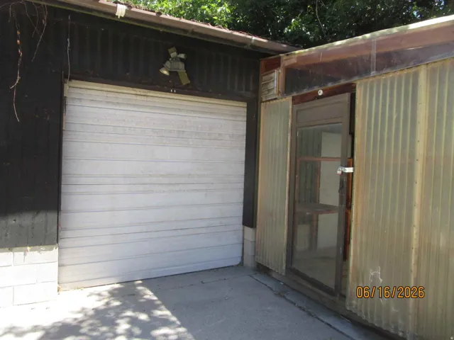 Single-car garage with a white roll-up door, featuring dark corrugated siding and a concrete foundation