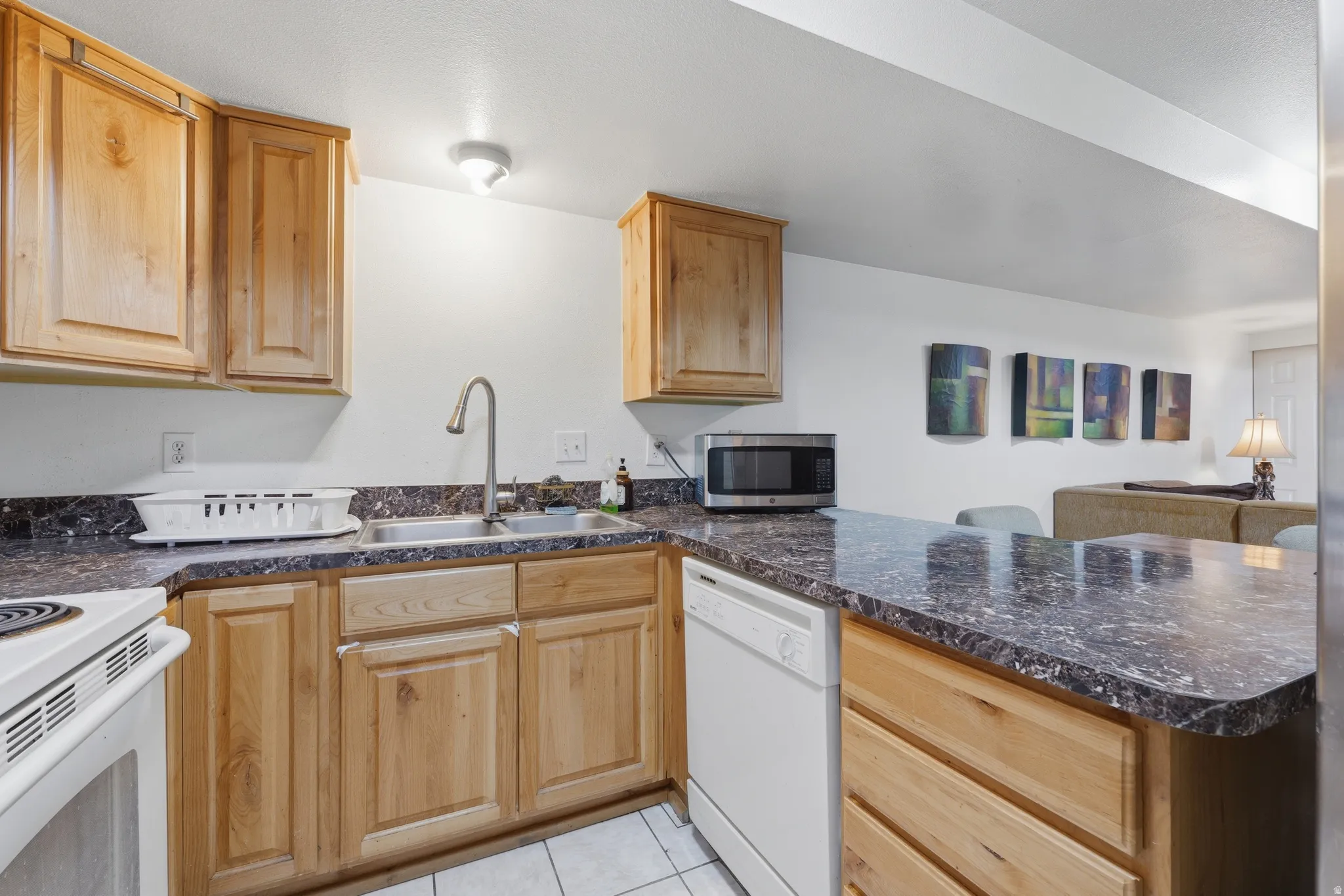 Kitchen featuring wood cabinetry, white appliances, a stainless steel sink with a gooseneck faucet, and dark speckled countertops