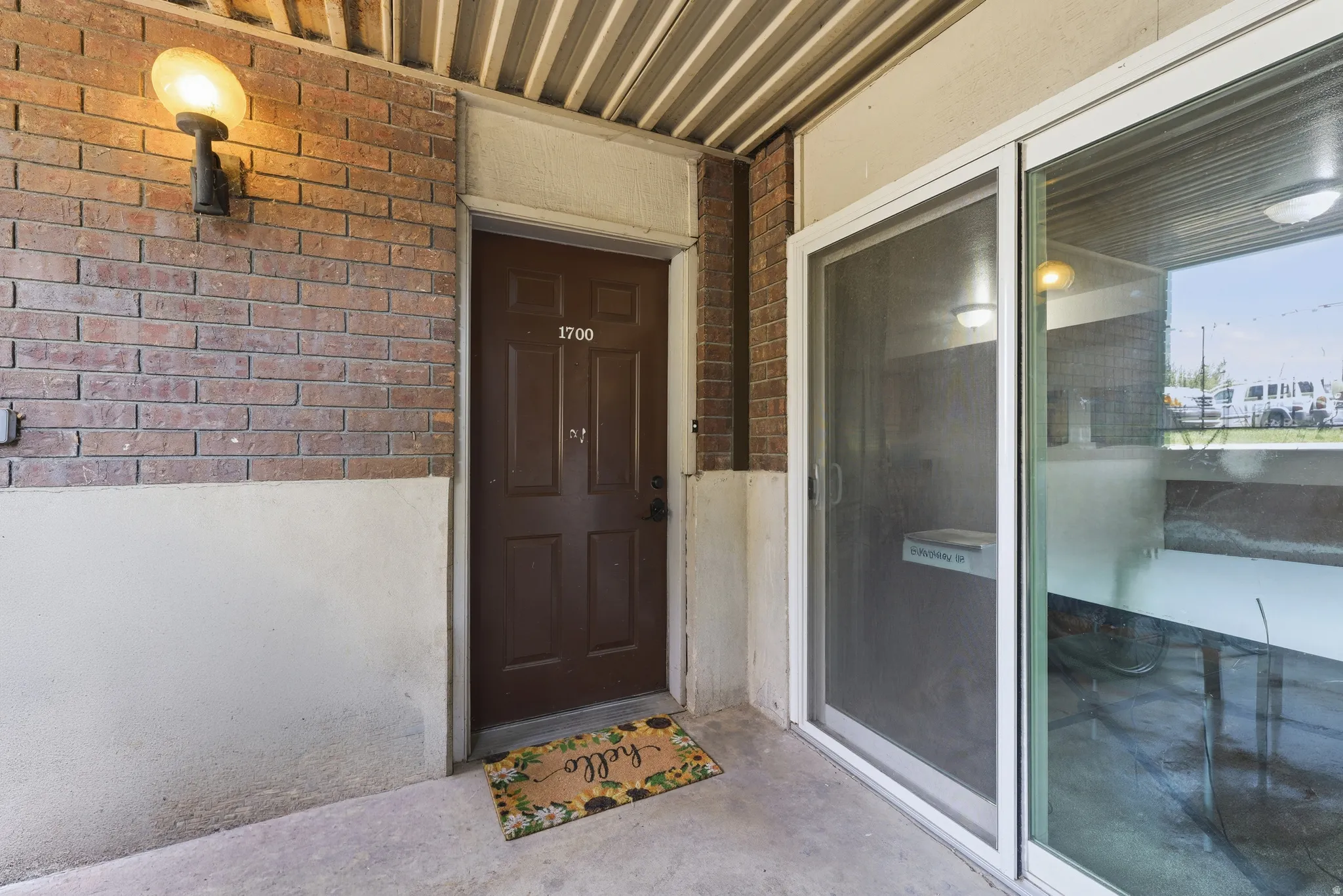 Brick exterior with an entryway sconce, a paneled brown door, and adjacent sliding glass doors