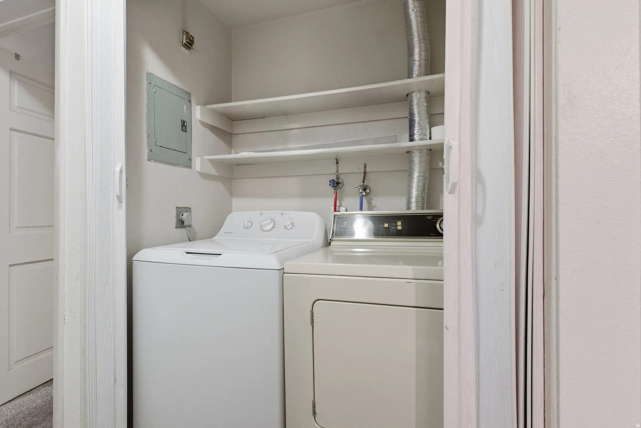 Dedicated laundry closet featuring a top-loading washing machine, front-loading dryer, and two built-in storage shelves
