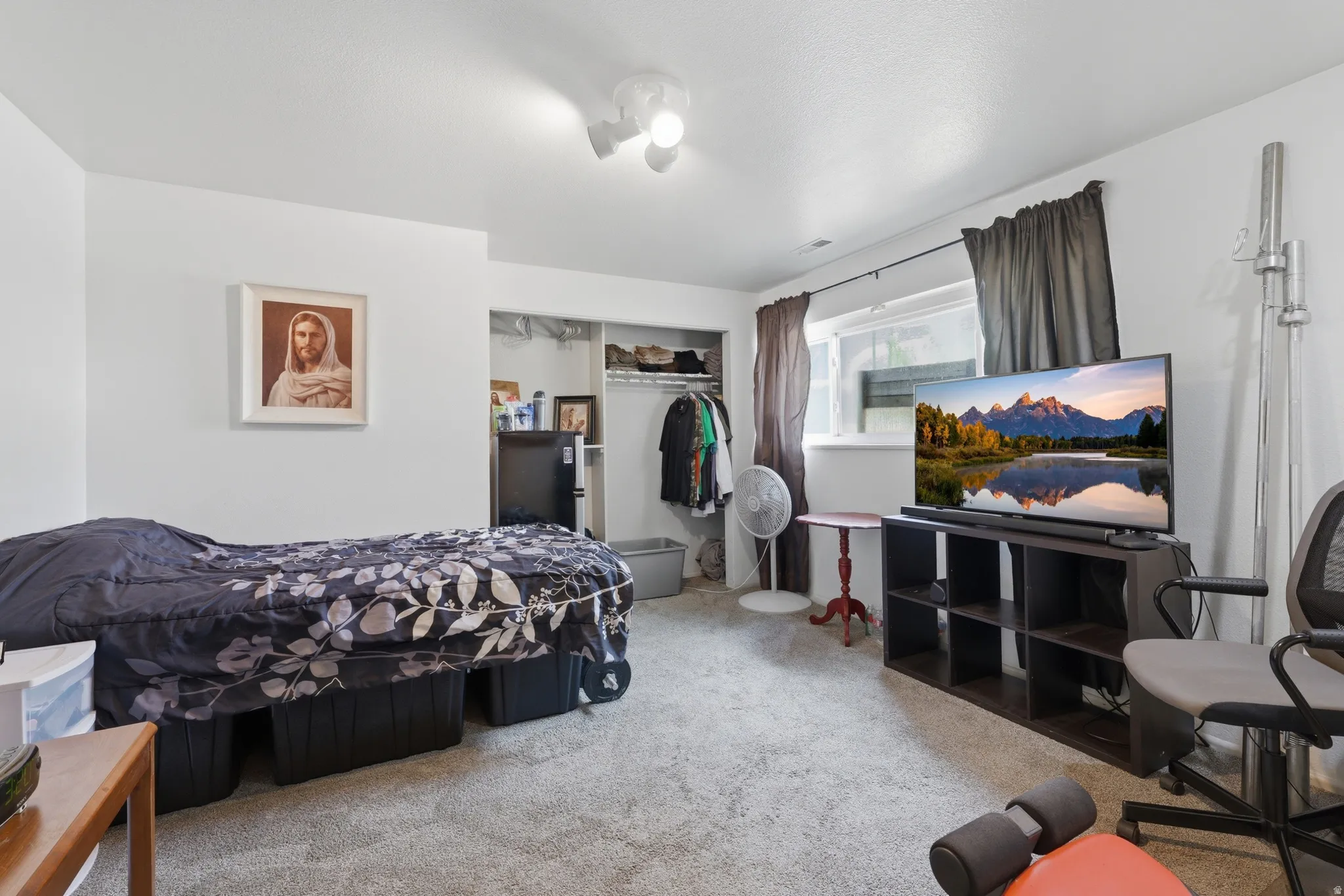 Carpeted room with white walls, a single window with dark drapes, and an open closet