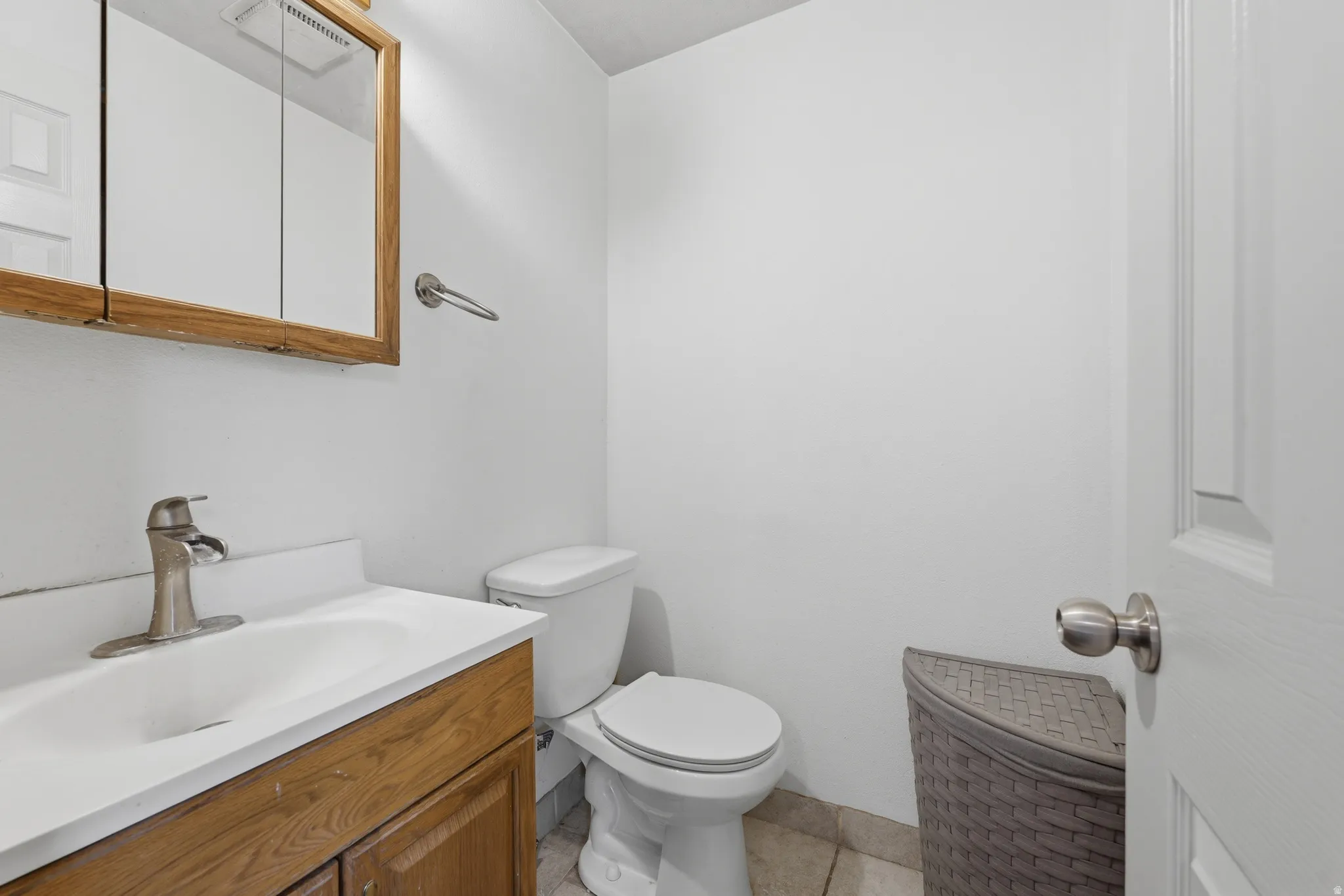 Bathroom featuring a wood-finish vanity with an integrated sink, a satin nickel faucet, a wood-framed medicine cabinet, and ceramic tile flooring