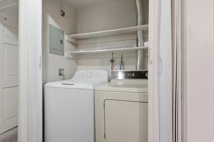 Dedicated laundry closet featuring a top-loading washing machine, front-loading dryer, and two built-in storage shelves