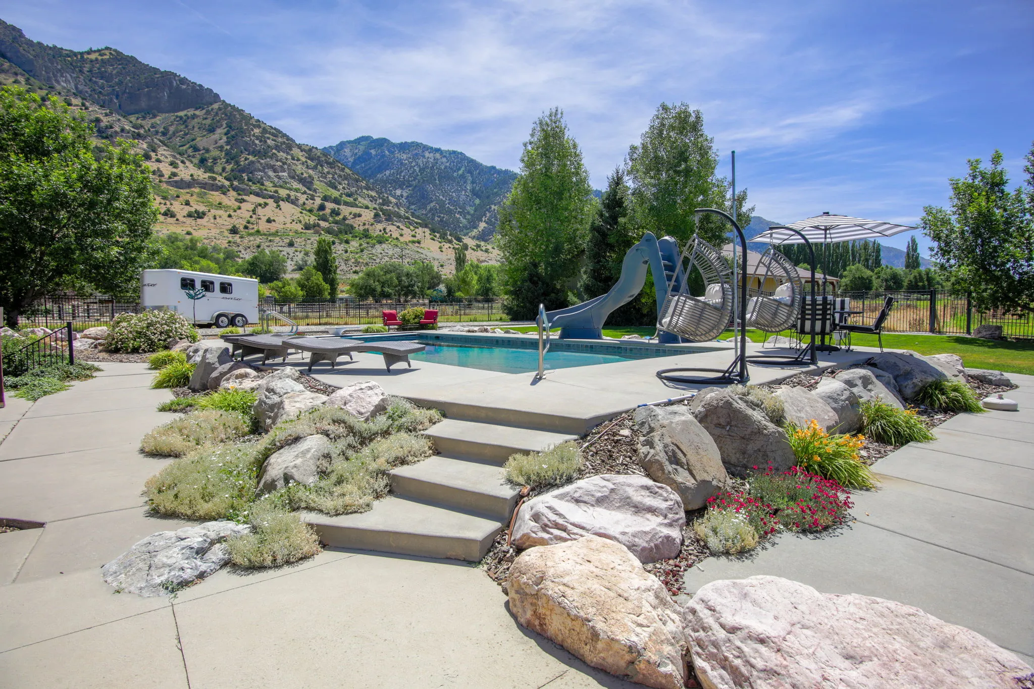 In-ground swimming pool featuring a water slide, concrete pool deck, and a surrounding rock garden with integrated steps
