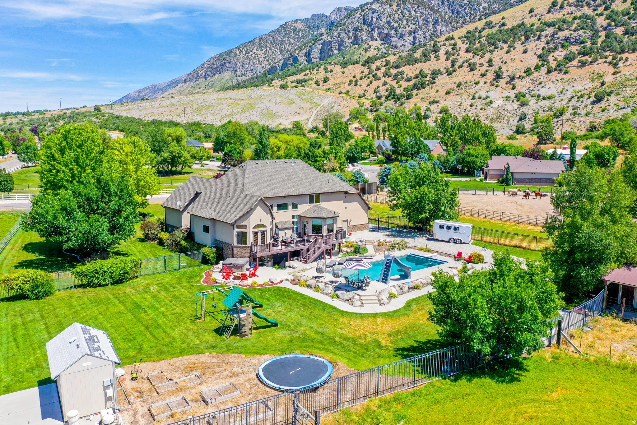 Expansive rear elevation featuring a multi-level deck, a swimming pool with a rock surround and slide, an outdoor play structure, and a fenced-in yard