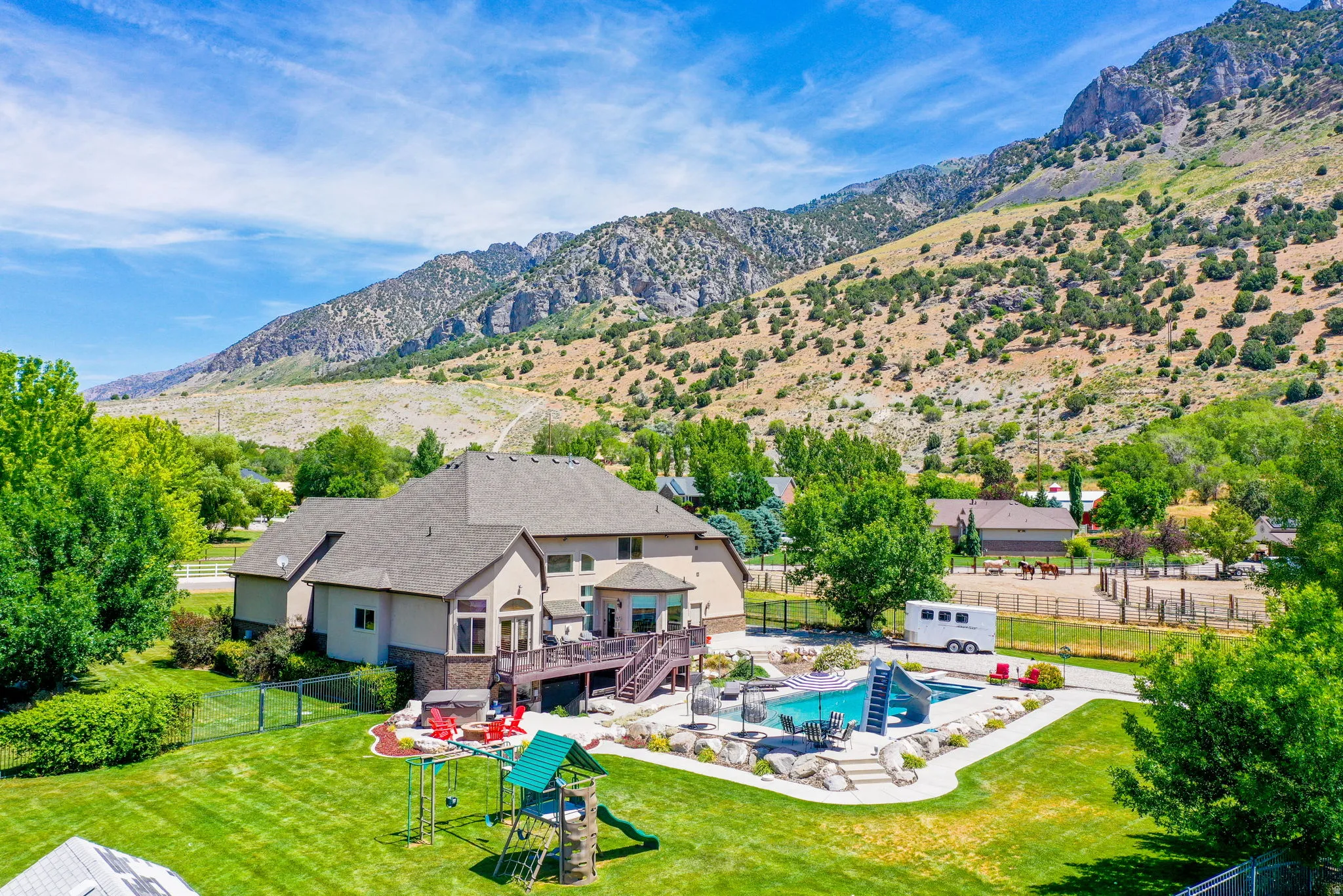 Expansive backyard featuring a large in-ground swimming pool with slide, a spacious deck, mature trees, and a mountain backdrop