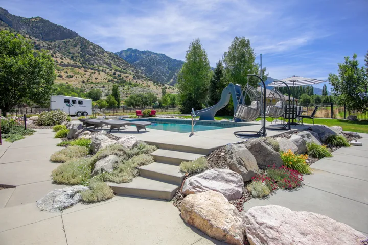 In-ground swimming pool featuring a water slide, concrete pool deck, and a surrounding rock garden with integrated steps