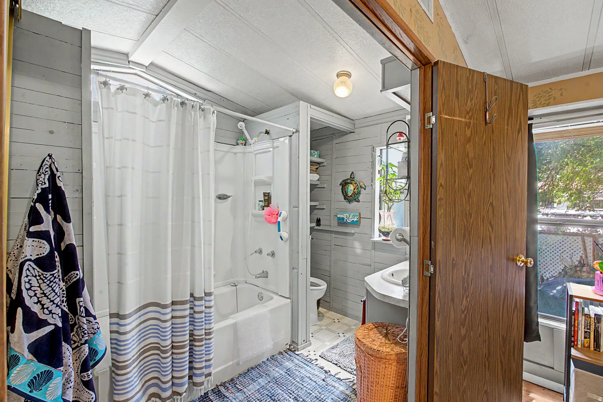 Compact bathroom featuring a white shower-over-tub combination with a wall-mounted showerhead, light gray wood-panel walls, and a white vanity with an integrated sink