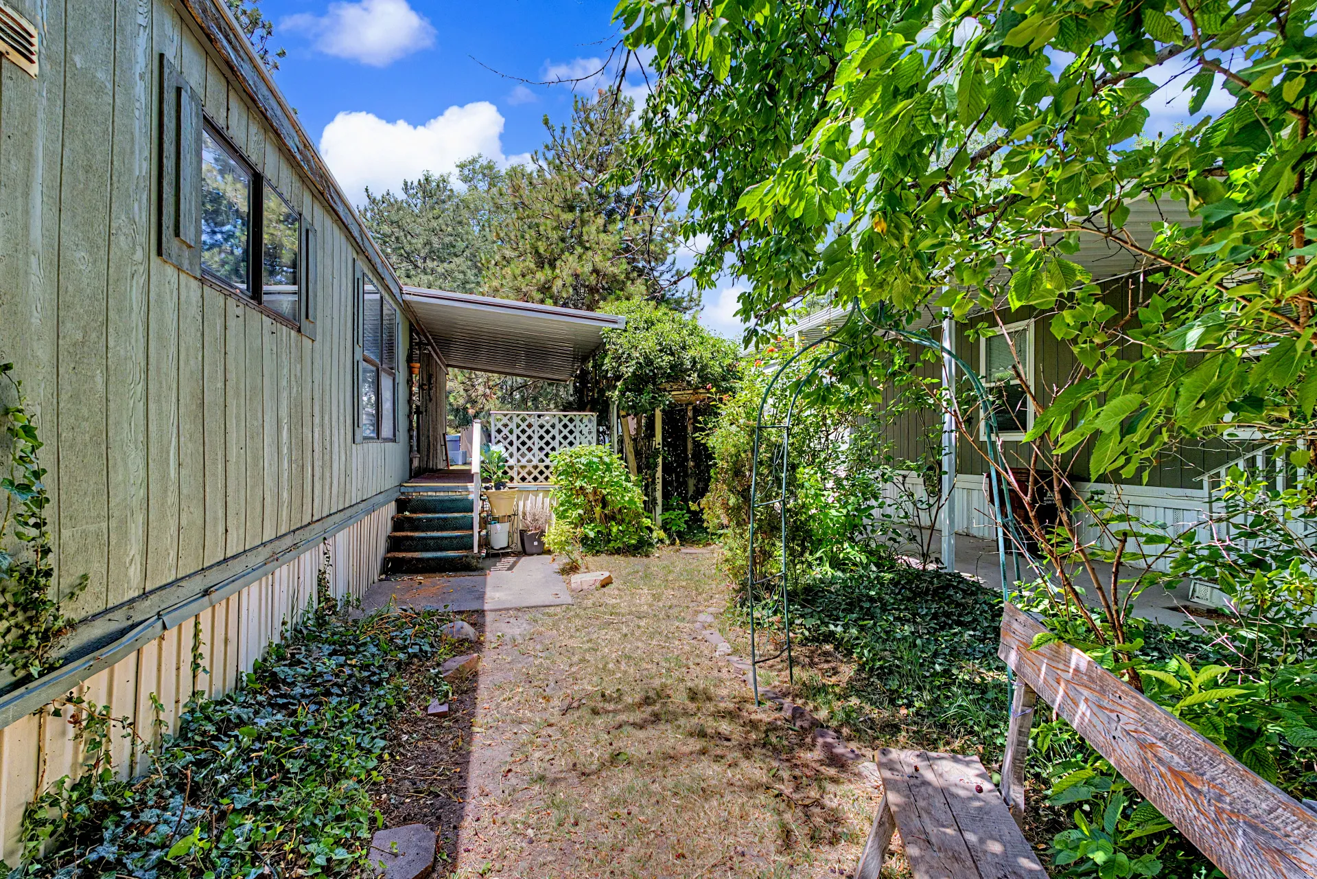 Side exterior featuring green siding, white trim, covered entryway, and a mature treed setting