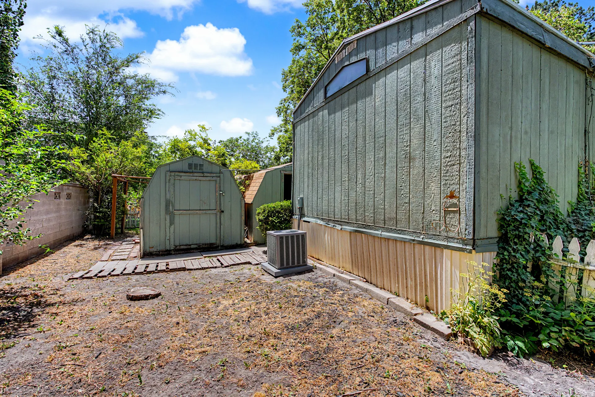 Exterior featuring two storage sheds, a concrete block privacy wall, and established perimeter landscaping