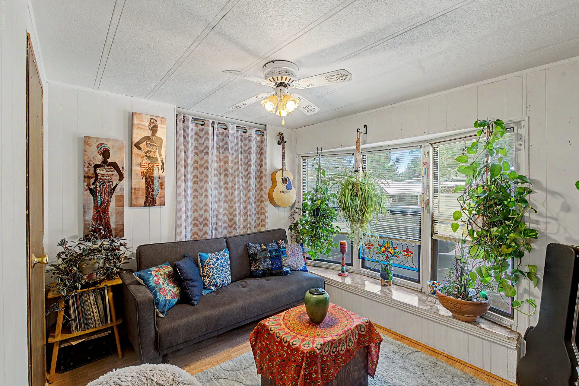 Living area featuring white paneled walls, a ceiling fan with integrated lighting, and multiple windows with horizontal blinds