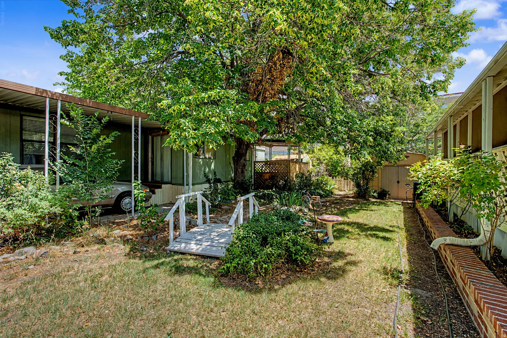 Shaded backyard featuring mature trees, a wooden bridge, and a storage shed