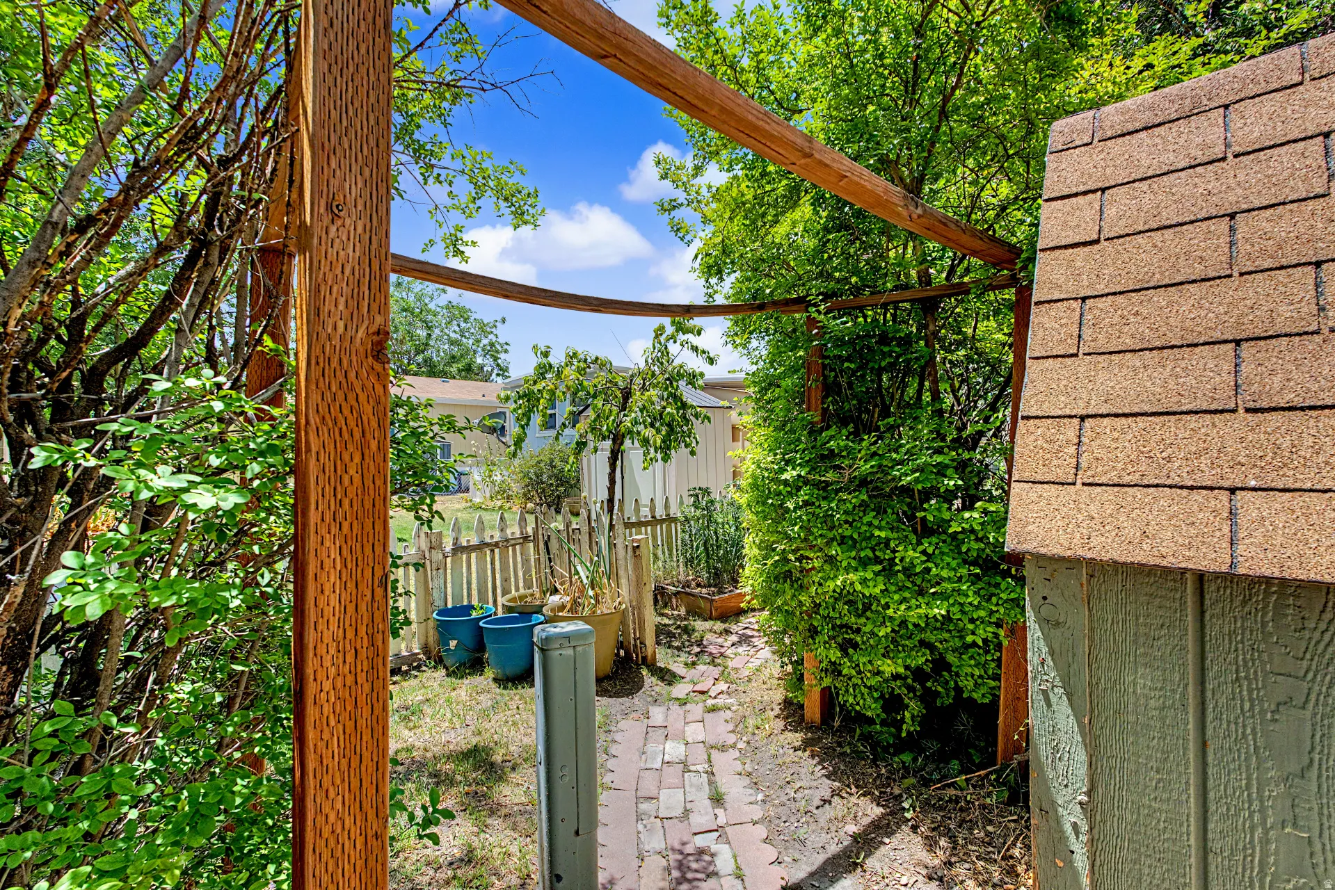Brick paver pathway with a wooden arbor leading to a fenced garden area