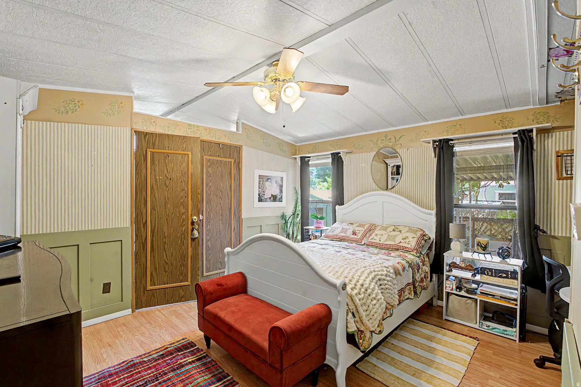 Spacious room featuring wood-finish flooring, two large windows with dark drapery, a multi-paneled ceiling, and a ceiling fan