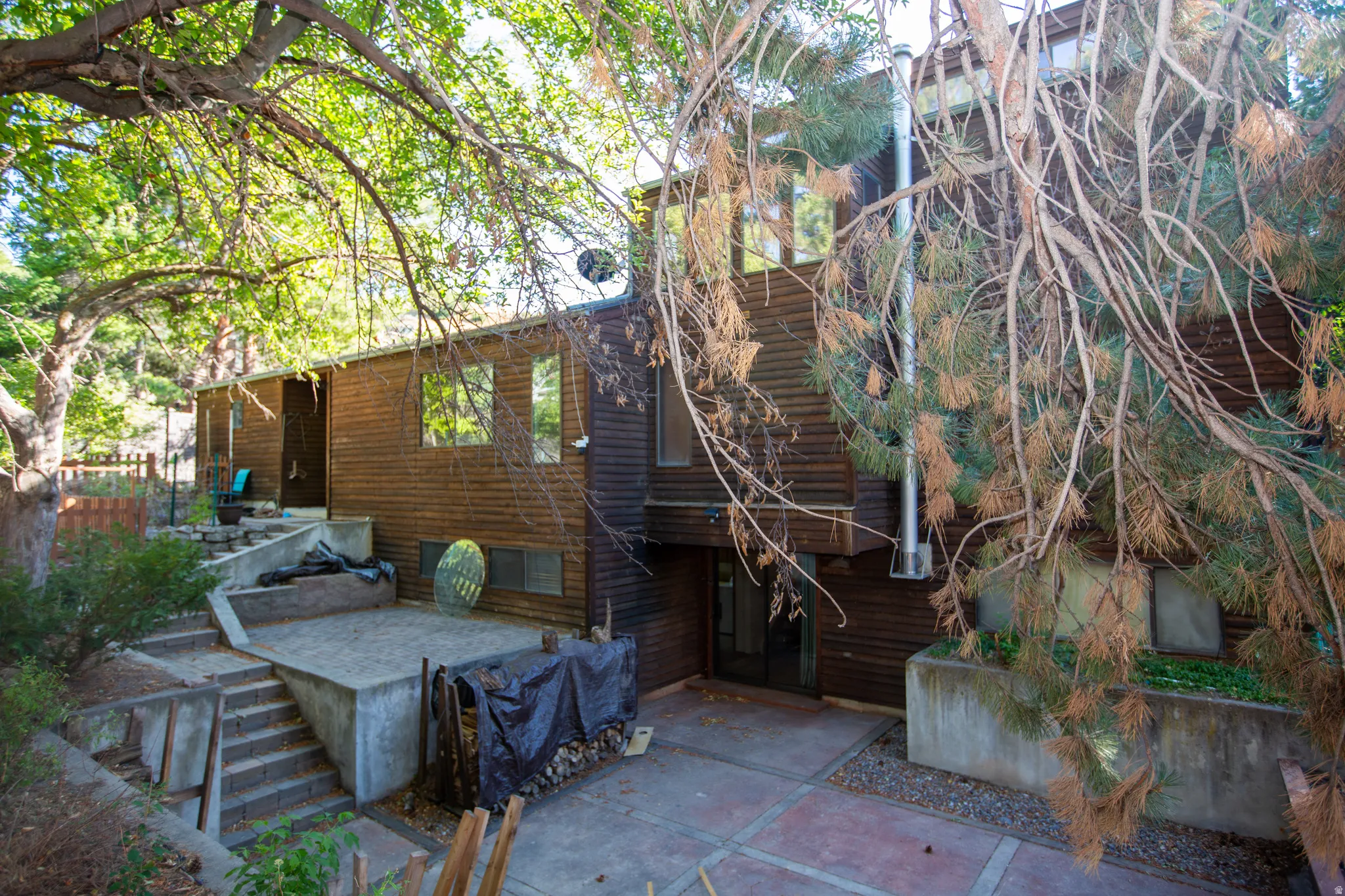 Wood-sided multi-level exterior featuring multiple window placements, a prominent chimney, and varied concrete patio areas