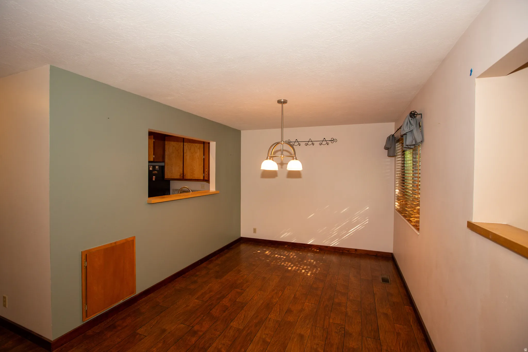 Dining room featuring wood-finish flooring, a pass-through window with wood trim, and a contemporary chandelier