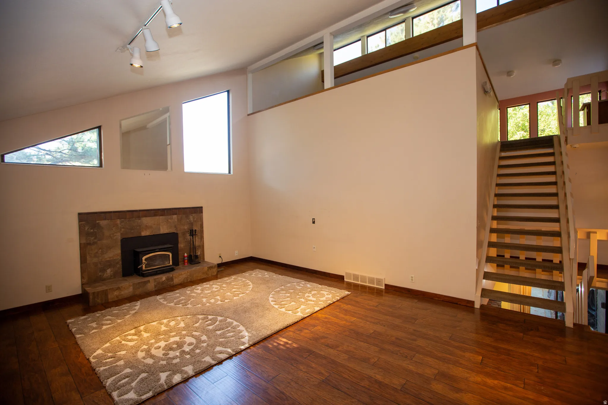 Great room featuring wood-finish flooring, a stone-clad fireplace with insert, a multi-level ceiling, and an open staircase with wood railings