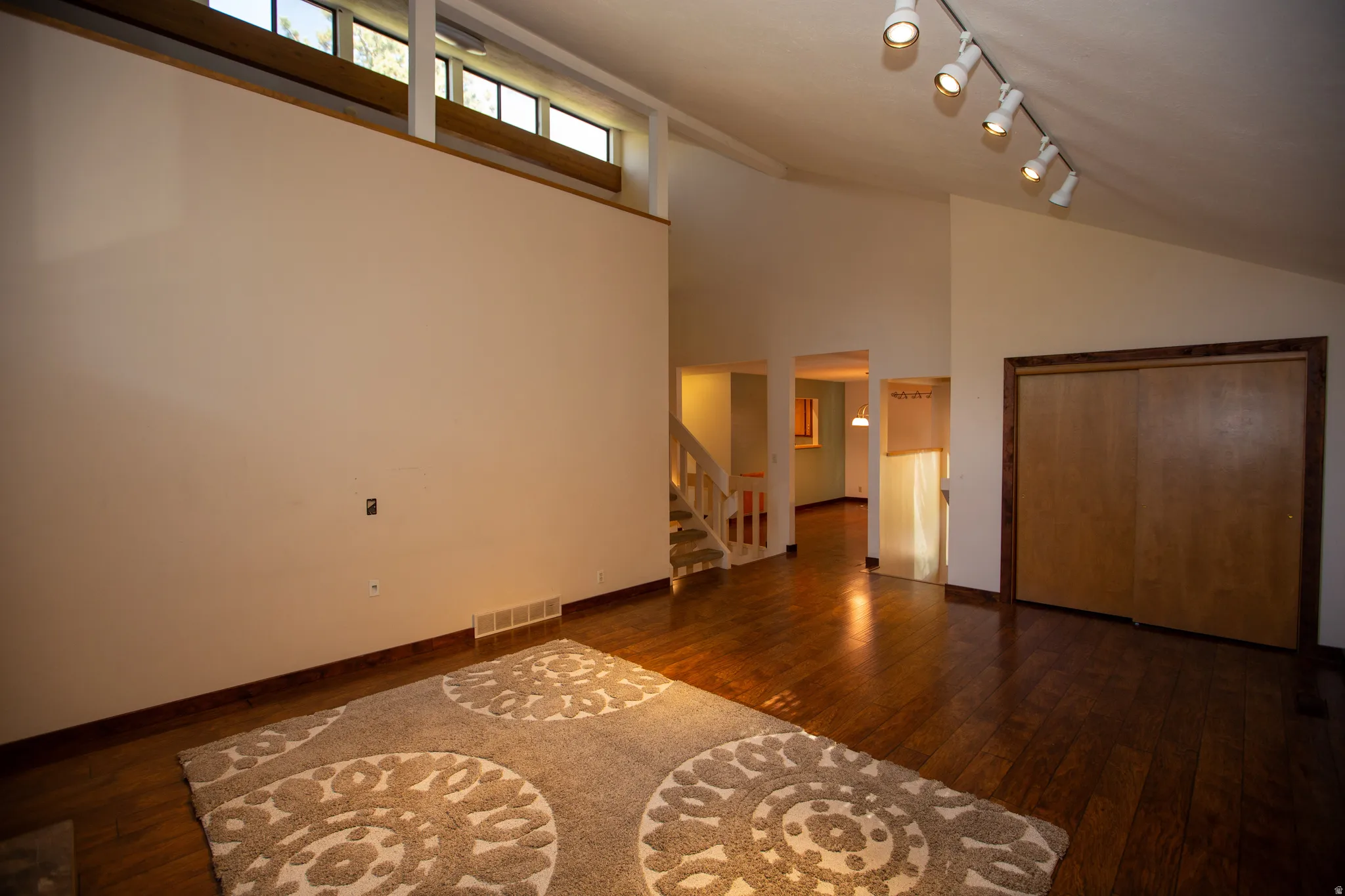 Vaulted ceilings with clerestory windows, wood-finish flooring, and track lighting fixtures