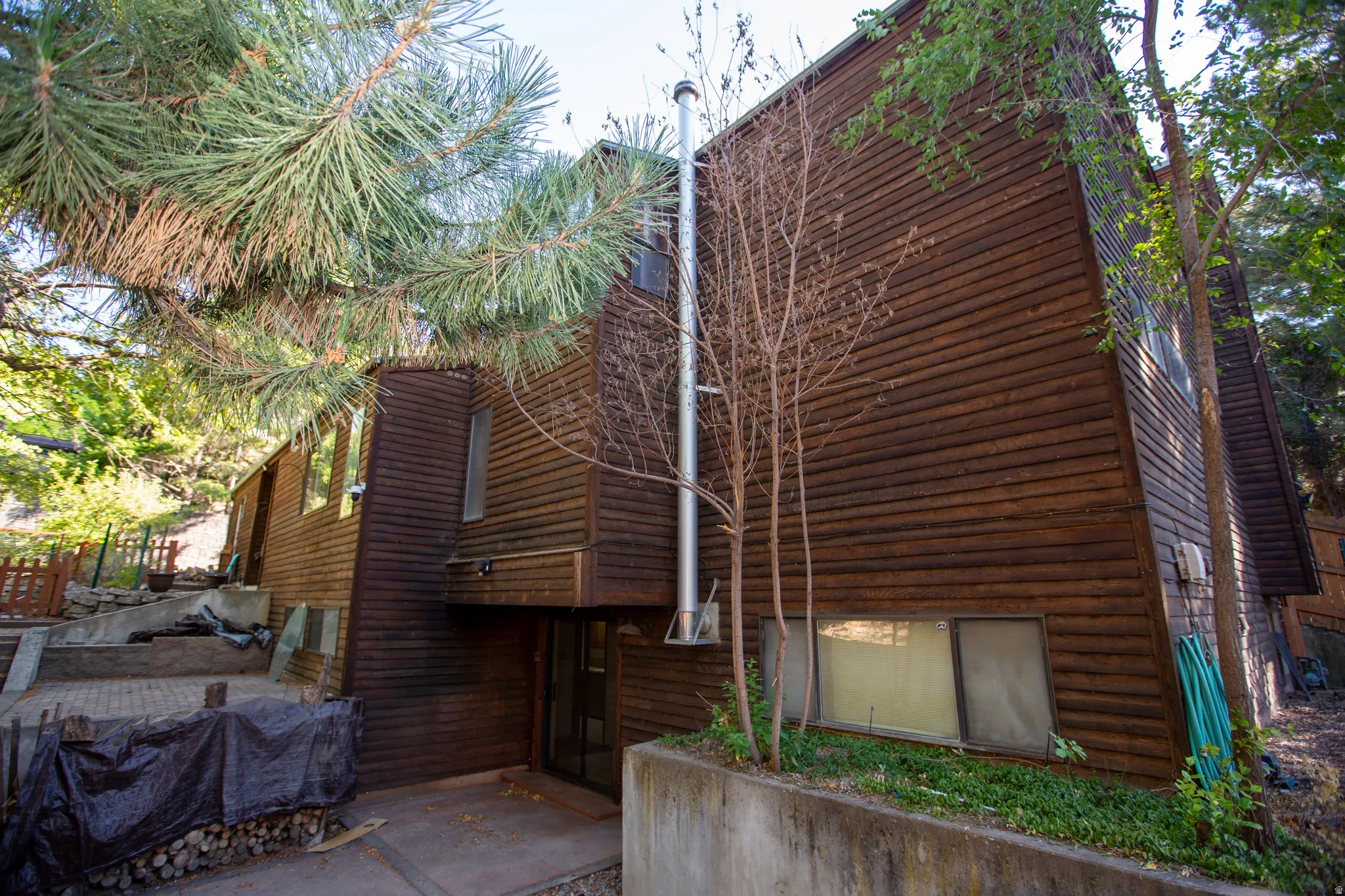 Terraced property featuring a wood-sided exterior, a prominent chimney, and mature trees