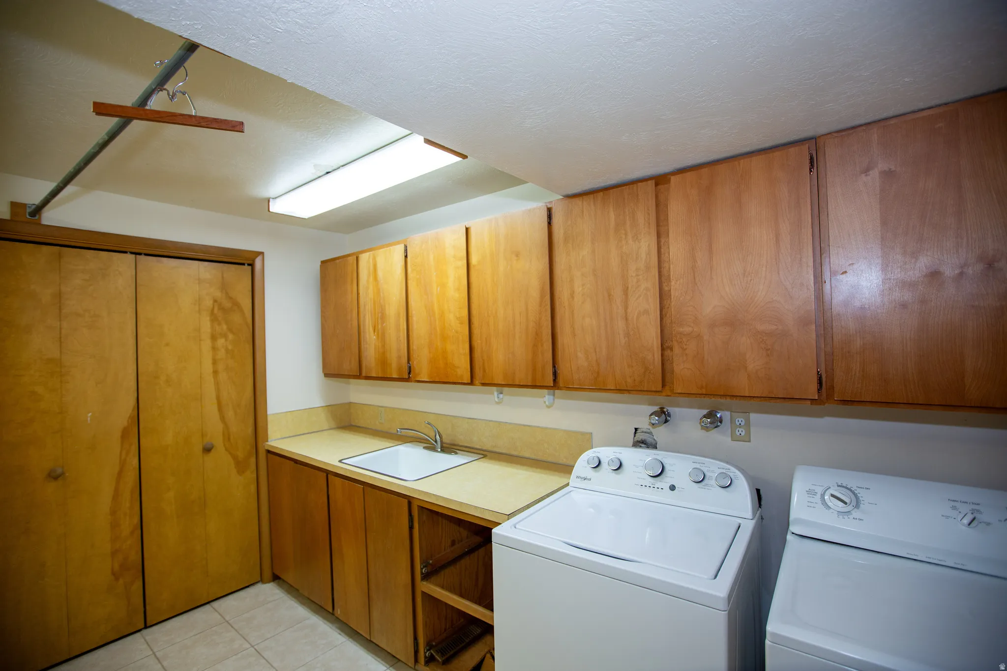 Laundry area featuring a utility sink, light wood-finish cabinetry, a bi-fold closet, and tiled flooring