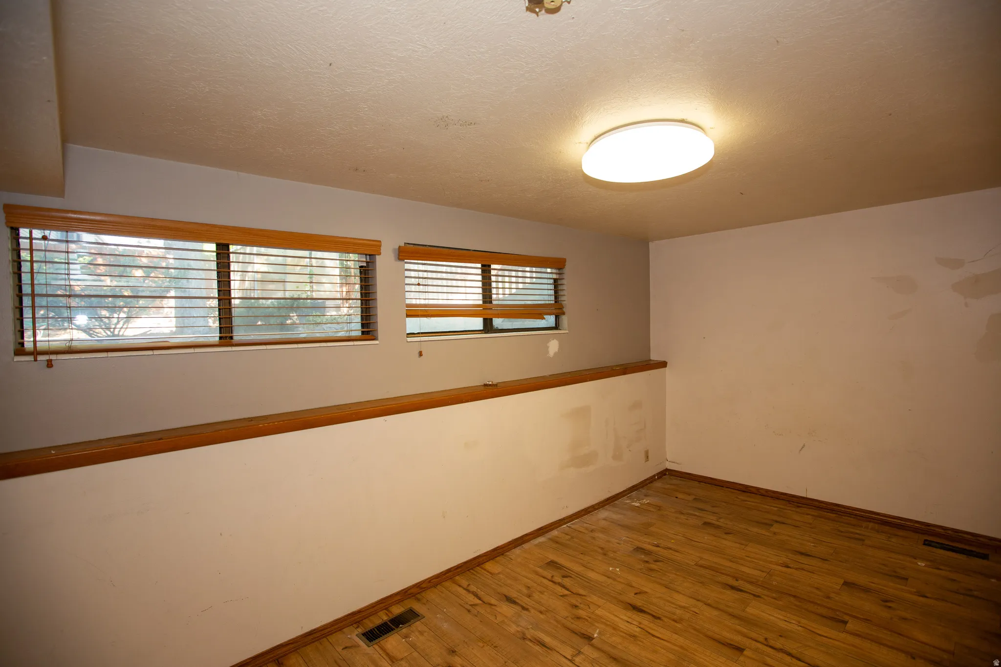 Bedroom featuring wood-finish flooring, two windows with wooden blinds, a wooden half-wall, and a ceiling-mounted flush light fixture