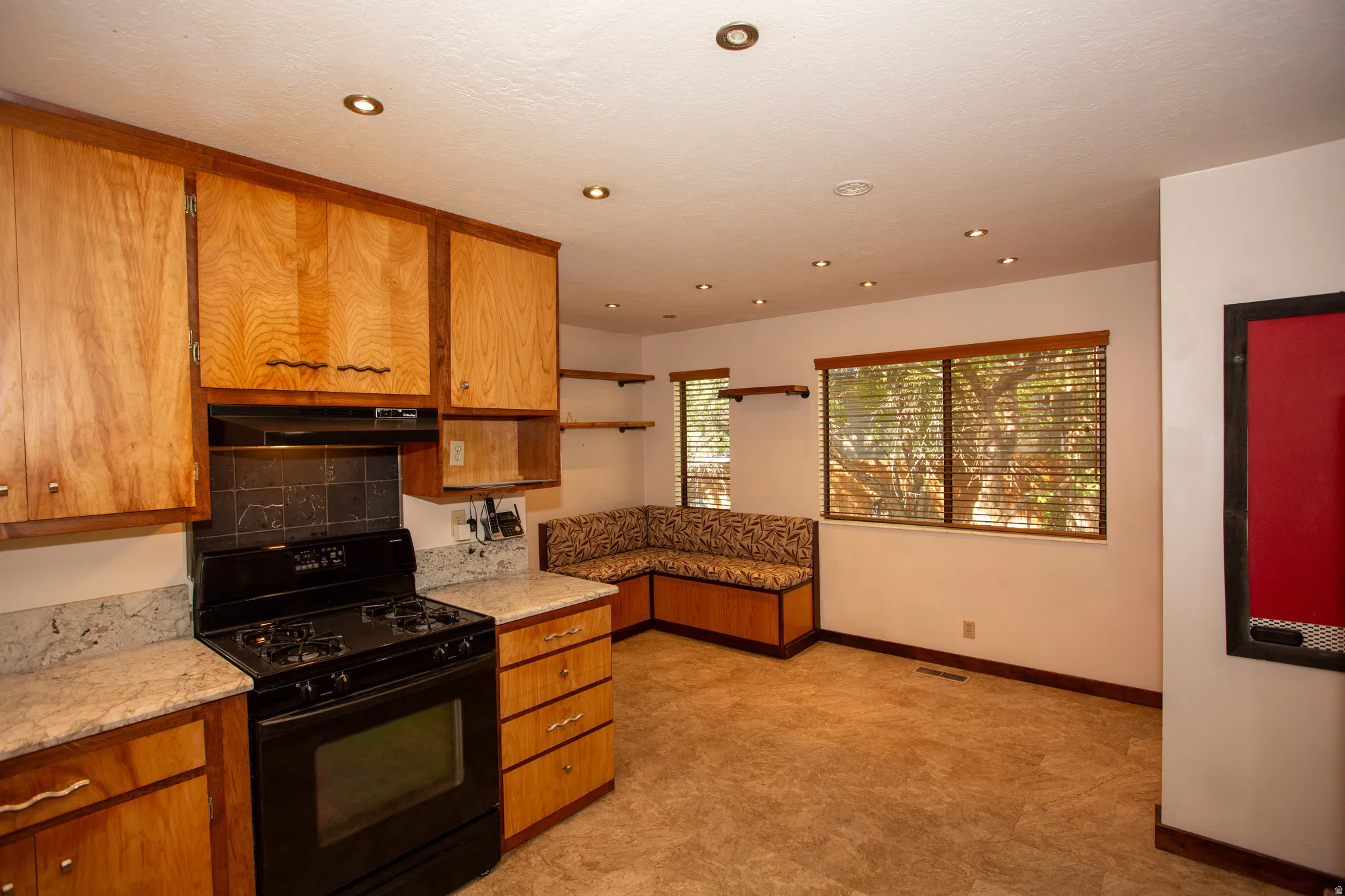 Kitchen space featuring natural wood cabinetry, light-toned granite countertops, and a black range