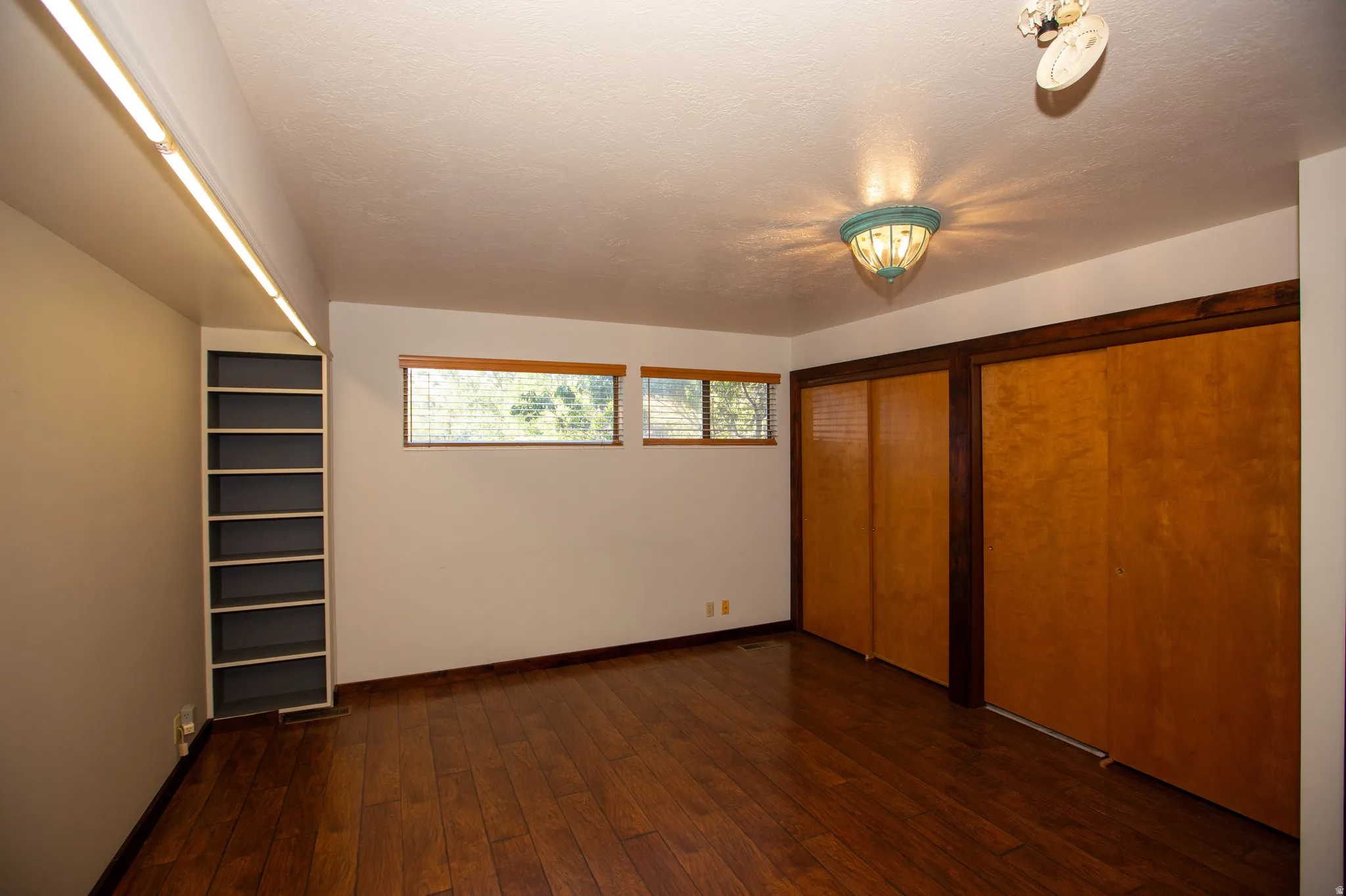 Primary Suite featuring wood-finish flooring, two large sliding closet doors, a built-in bookshelf, and multiple windows with wood blinds