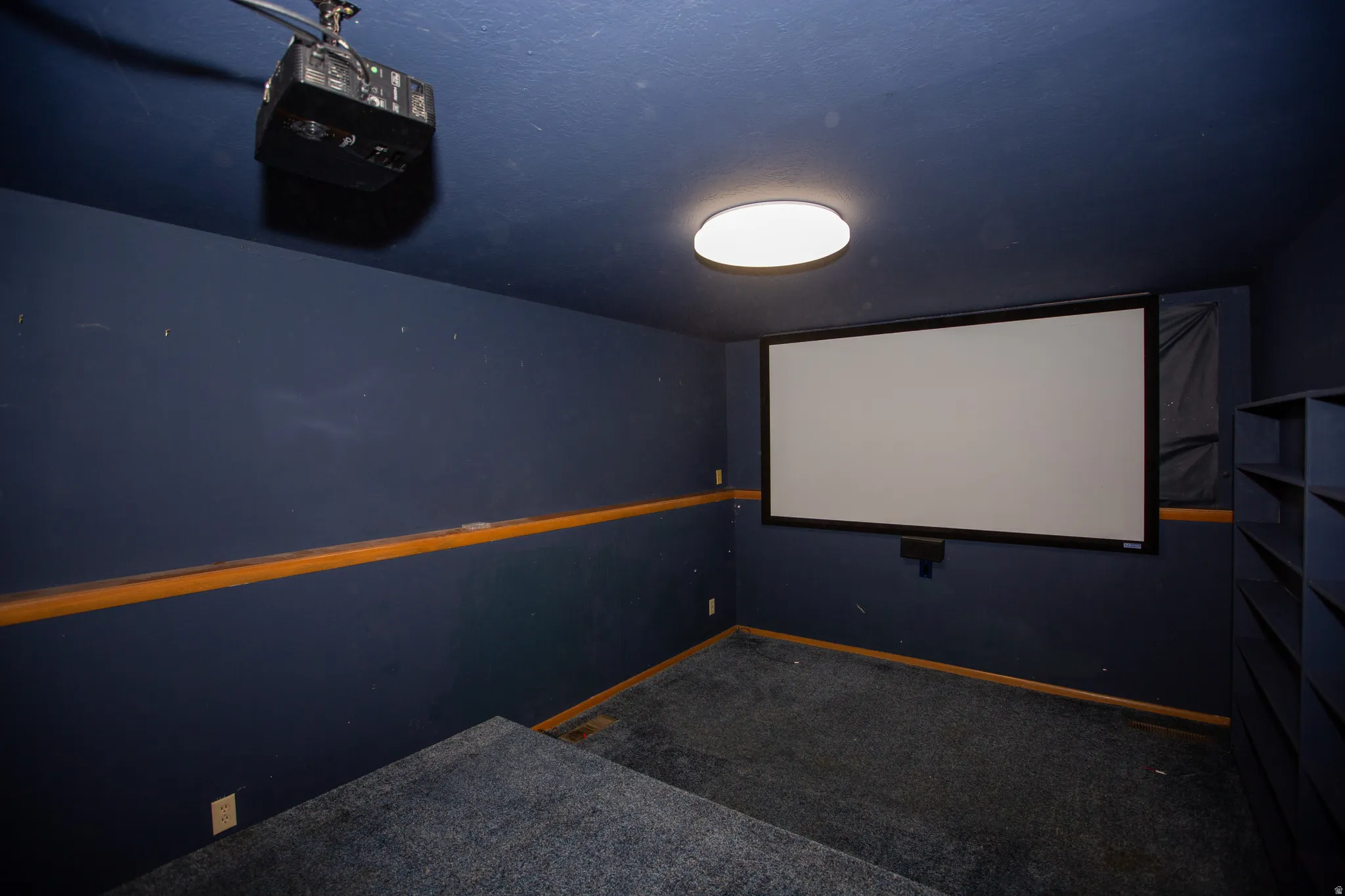 Dedicated theater room featuring a large projection screen, ceiling-mounted projector, and built-in shelving