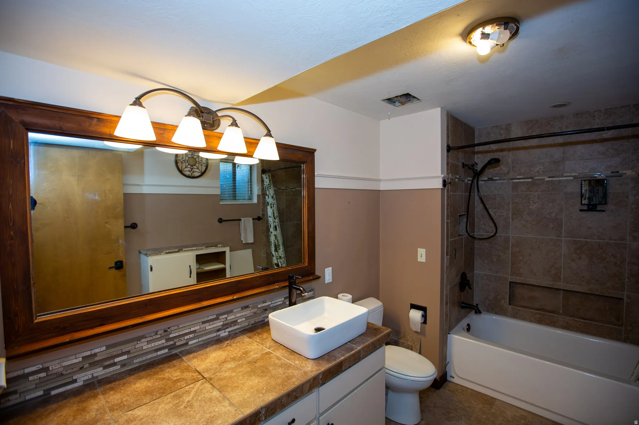Full bathroom featuring a wood-framed mirror, a rectangular vessel sink with a dark faucet, and a tiled countertop