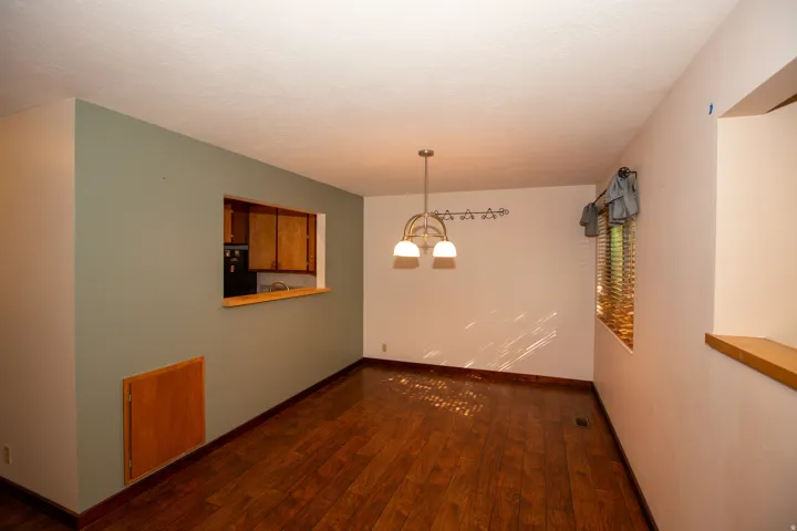 Dining room featuring wood-finish flooring, a pass-through window with wood trim, and a contemporary chandelier