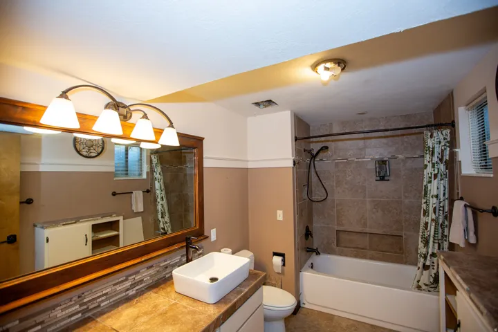 Full bathroom featuring a built-in tub with tile surround, a vessel sink on a tiled countertop, a wooden framed mirror, and a four-light vanity fixture