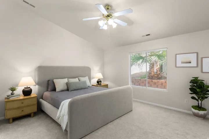 Sloped ceiling with an attached ceiling fan, large window with horizontal blinds, neutral-toned wall paint, and light-colored carpet