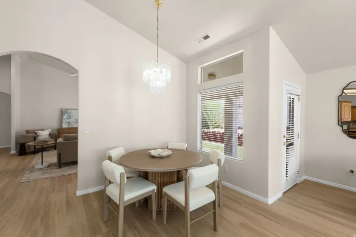 Wood-finish flooring, arched doorway, clear glass chandelier, white walls, and a window with blinds