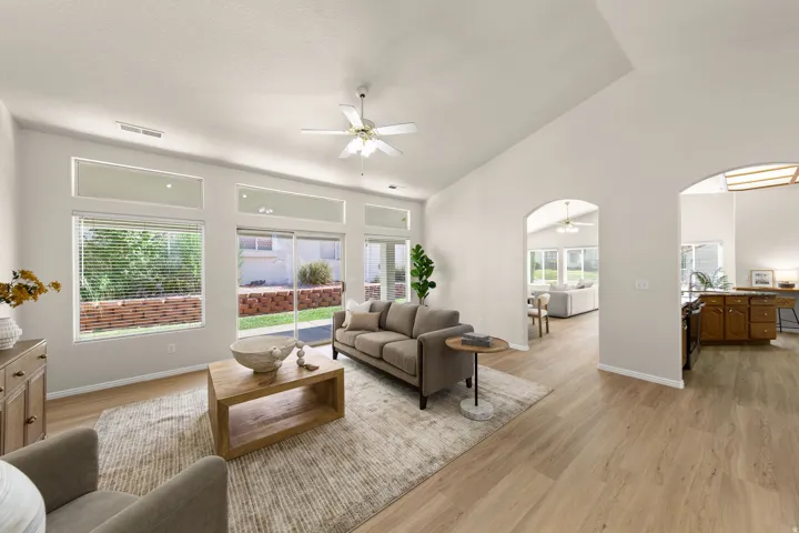 Vaulted ceiling, ceiling fan, wood-finish flooring, multiple arched doorways, and a wall of windows with transom panels