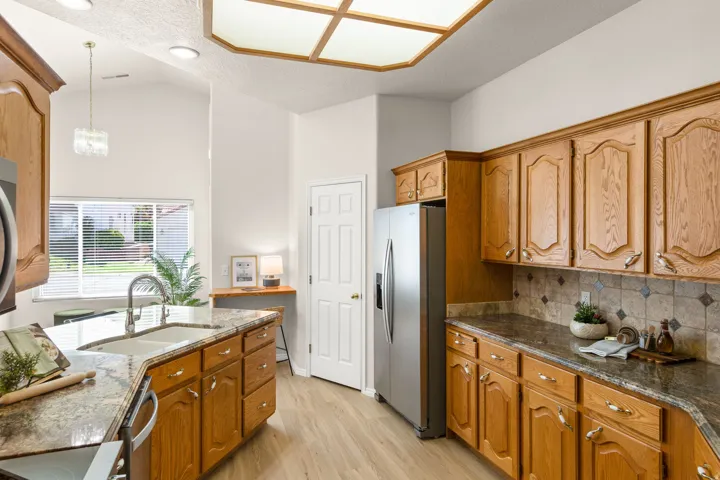 Wood-finish flooring, ample wood cabinetry, patterned tile backsplash, and stone-finish countertops