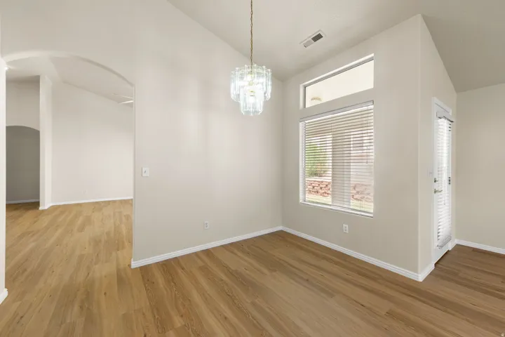 Room featuring wood-finish flooring, a contemporary chandelier, arched entryway, a large window with blinds, and a glass-paneled door